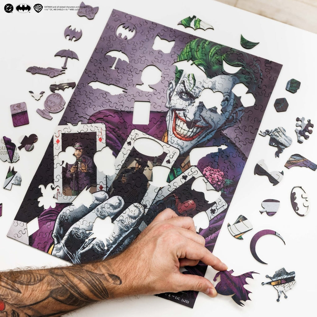 Jigsaw puzzle of the Joker from Batman with a hand arranging pieces on a white surface.
