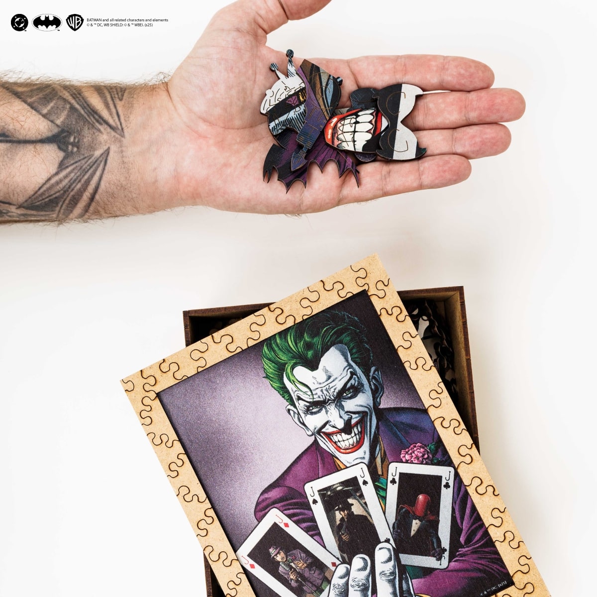 Hand holding Joker-themed decorative items with a puzzle featuring the Joker on a white background.