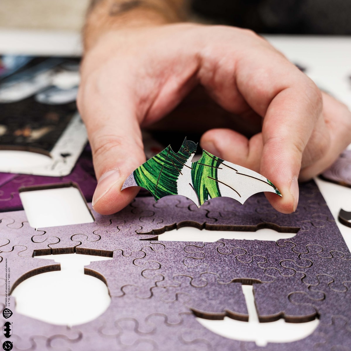 Hand placing a puzzle piece with green leaves on a purple puzzle piece.