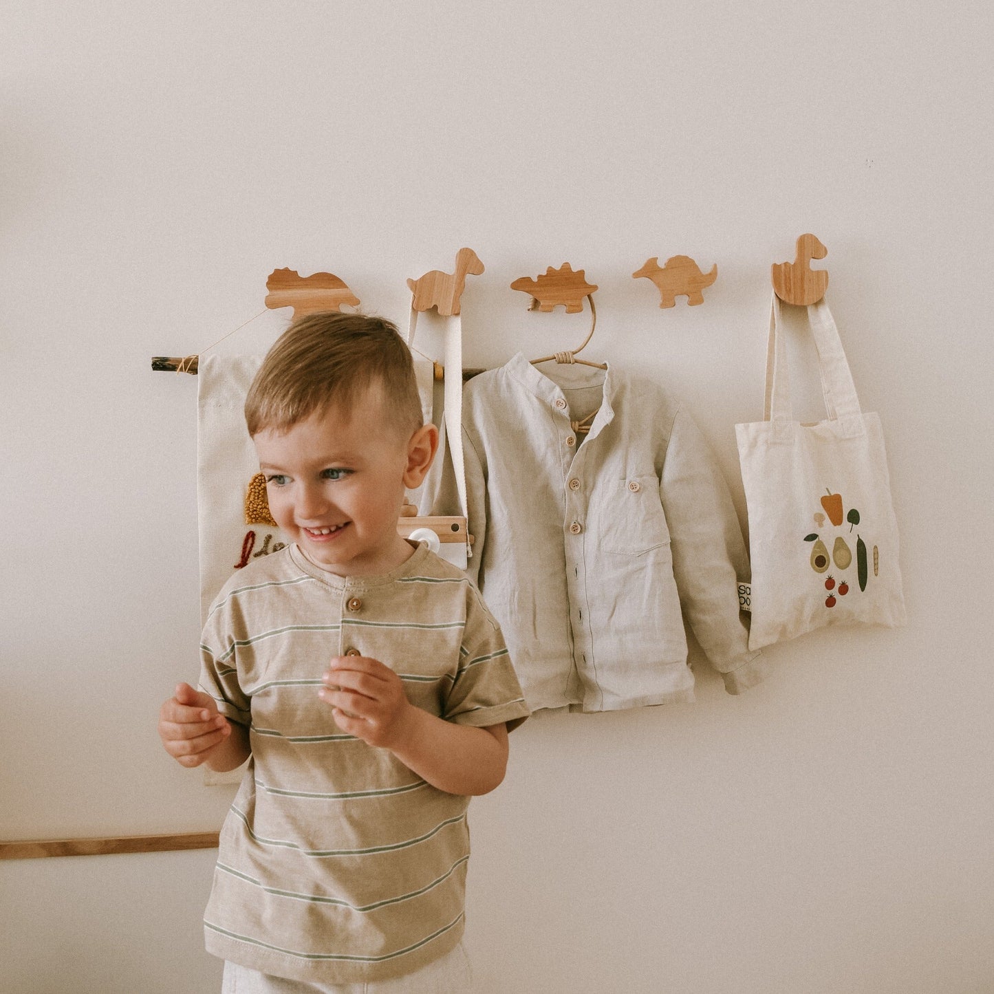 Child standing in front of a wall with clothes and bags hanging on hooks