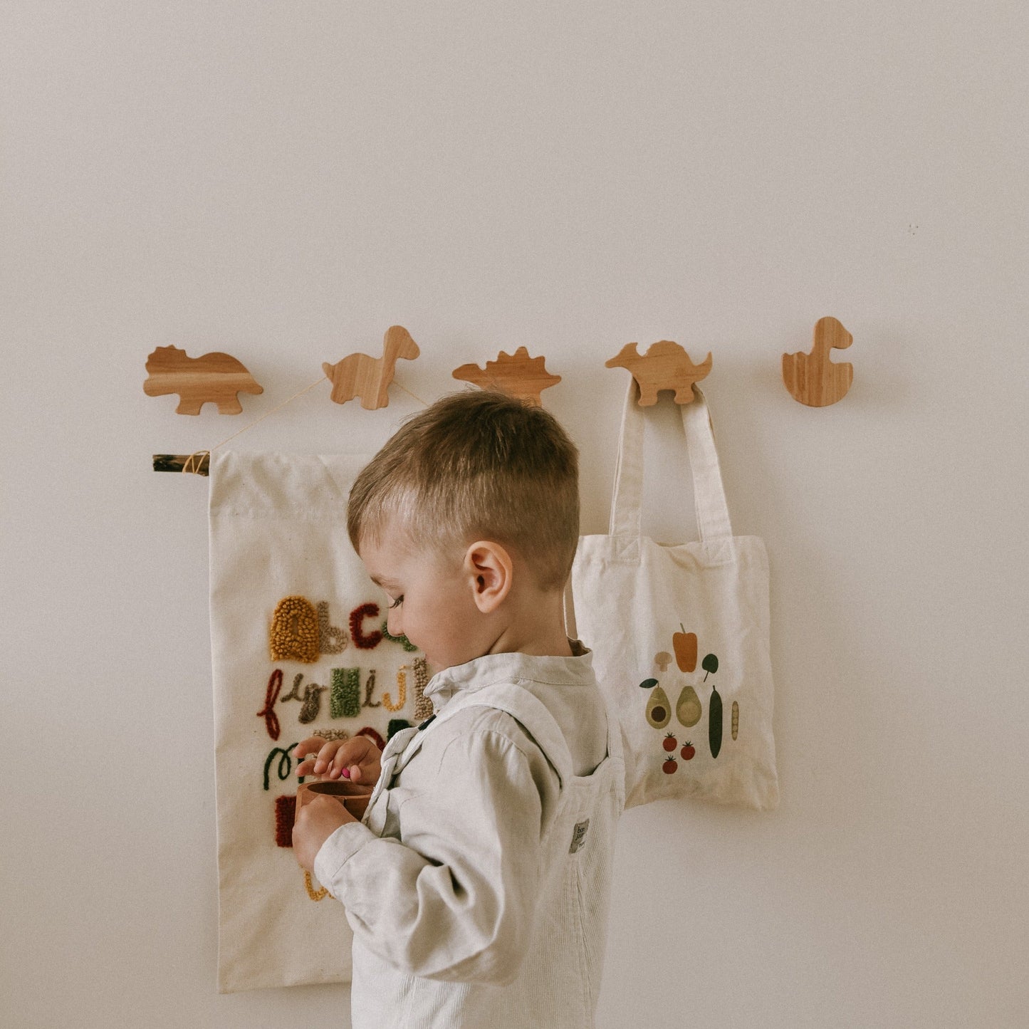 Child interacting with a wall-mounted fabric with alphabet letters, surrounded by wooden animal hooks.