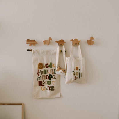 Three tote bags with animal designs hanging on wooden hooks against a white wall.