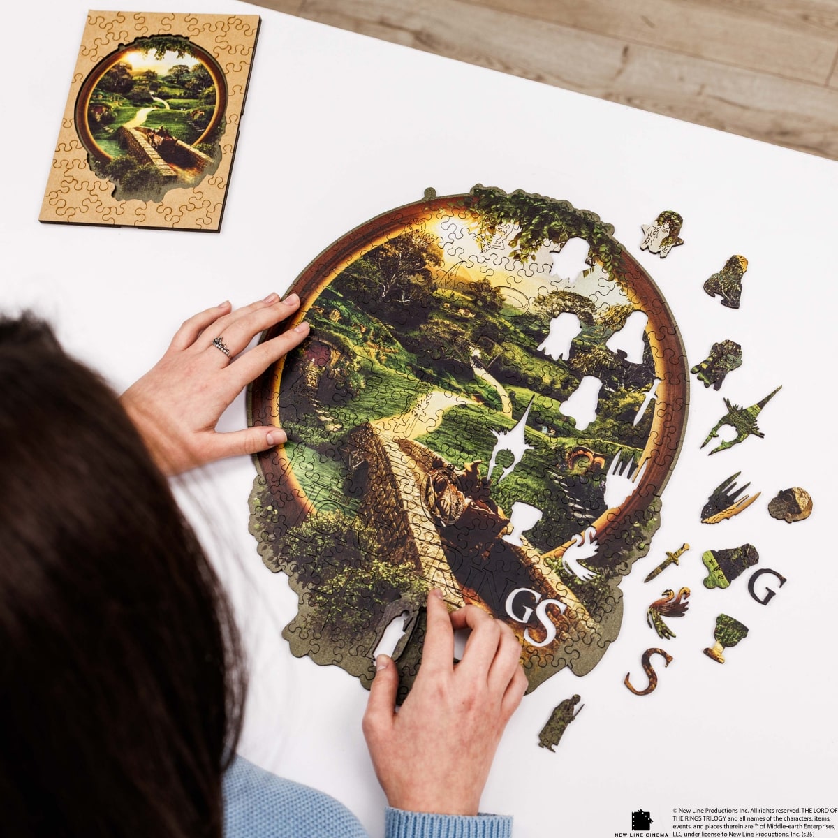 Person assembling a puzzle of a nature scene with a completed section on a white surface.