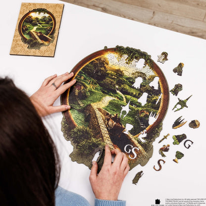 Person assembling a puzzle of a nature scene with a completed section on a white surface.