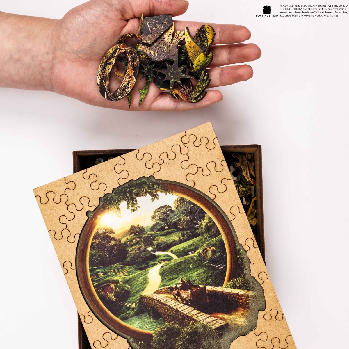 Hand holding puzzle pieces with a completed puzzle of a scenic landscape on a white background