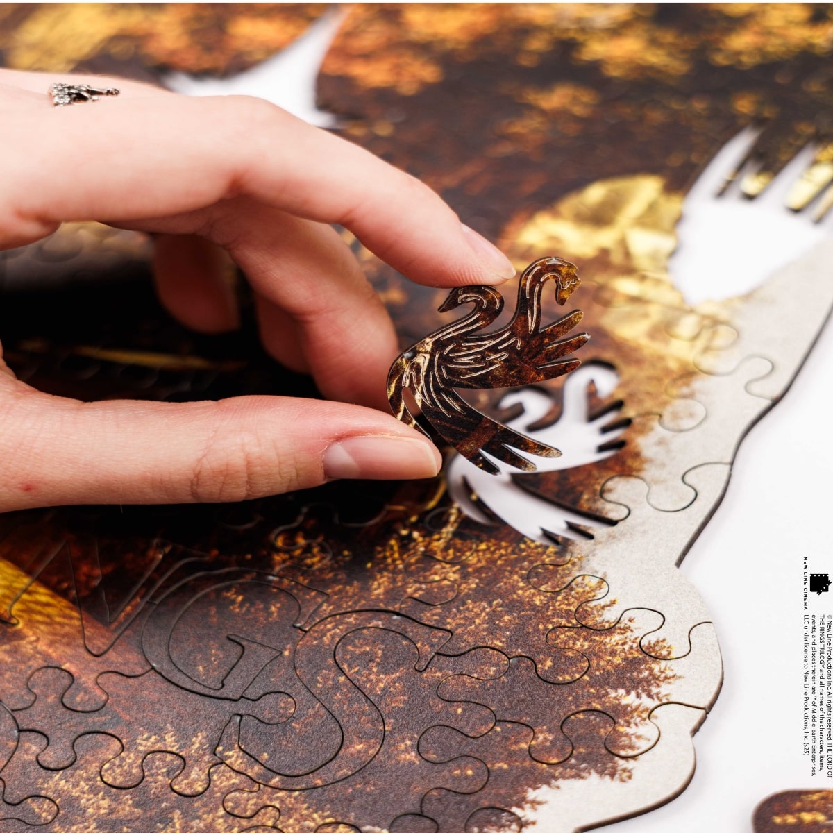 Hand holding a metallic dragon puzzle piece over a partially completed puzzle.