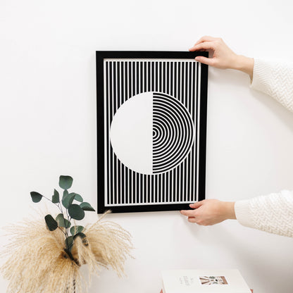 Person holding a black and white geometric art print on a light surface with decorative elements.