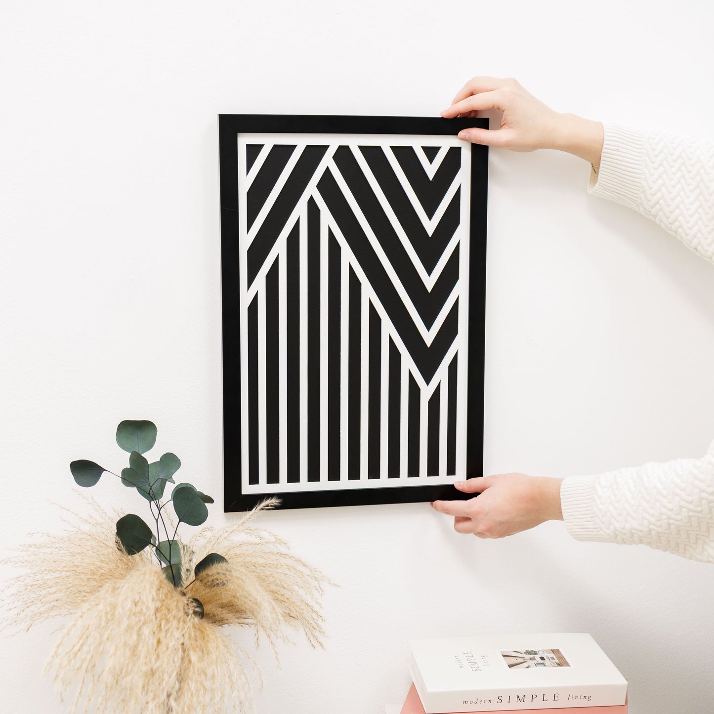 Person holding a black and white geometric art print on a light surface with decorative items.