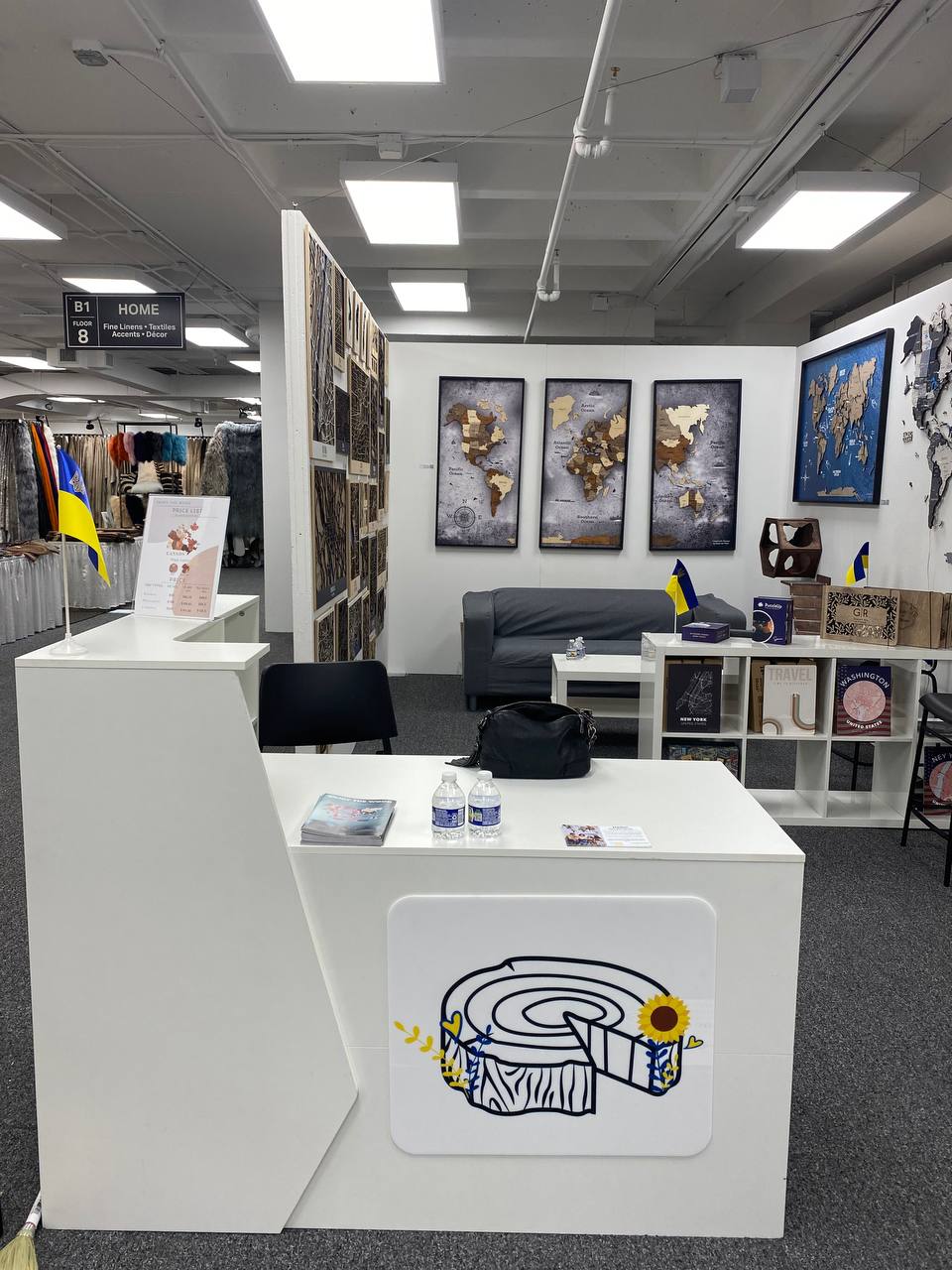 Modern office interior with a white reception desk featuring a logo, surrounded by office furniture and decor.