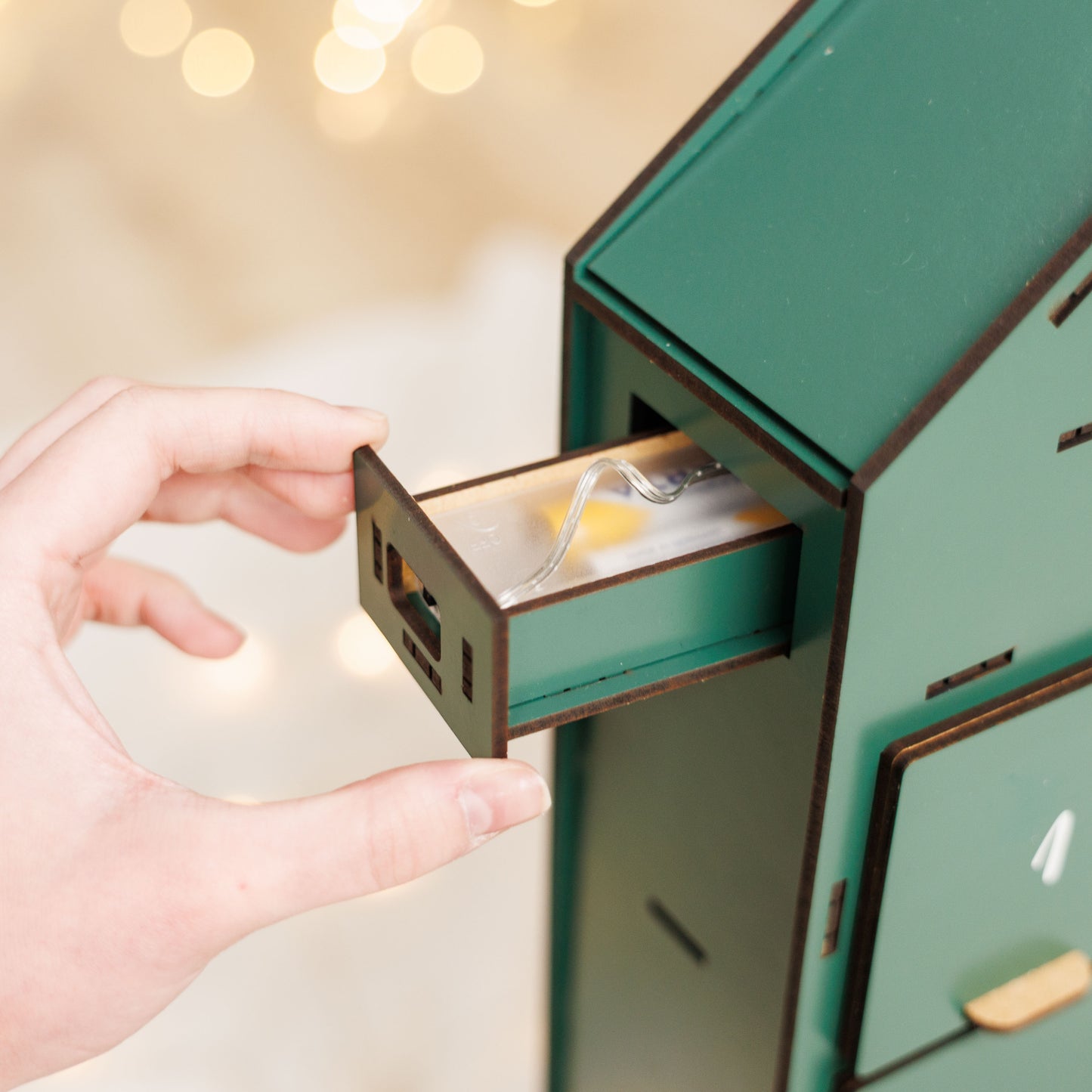 Hand opening a small green cabinet with a drawer, blurred lights in the background