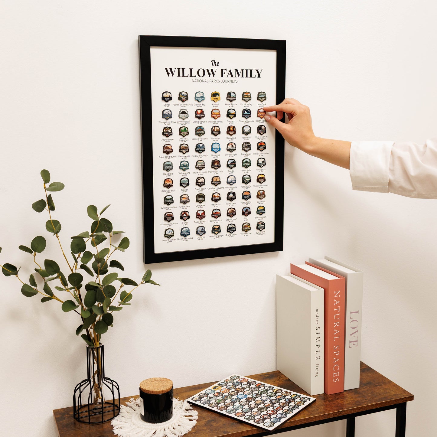 Person interacting with a framed family crest chart on a wall next to a table with books and decor.