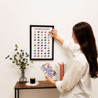 Woman hanging a framed print of flags on a wall next to a table with decor items.