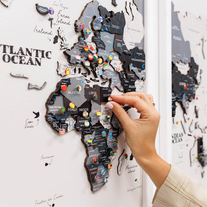 World map with pins on a white wall, hand placing a pin.