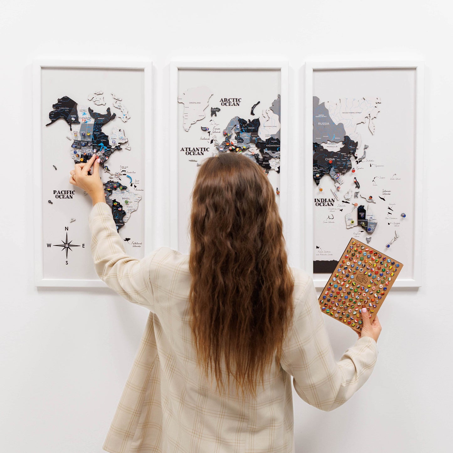 Woman holding a colorful book in front of framed world maps on a white wall