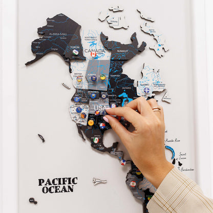 Map of North America with pins marking locations, being held by a hand.