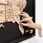 Hand placing a pin on a wooden map of the United States with a black background