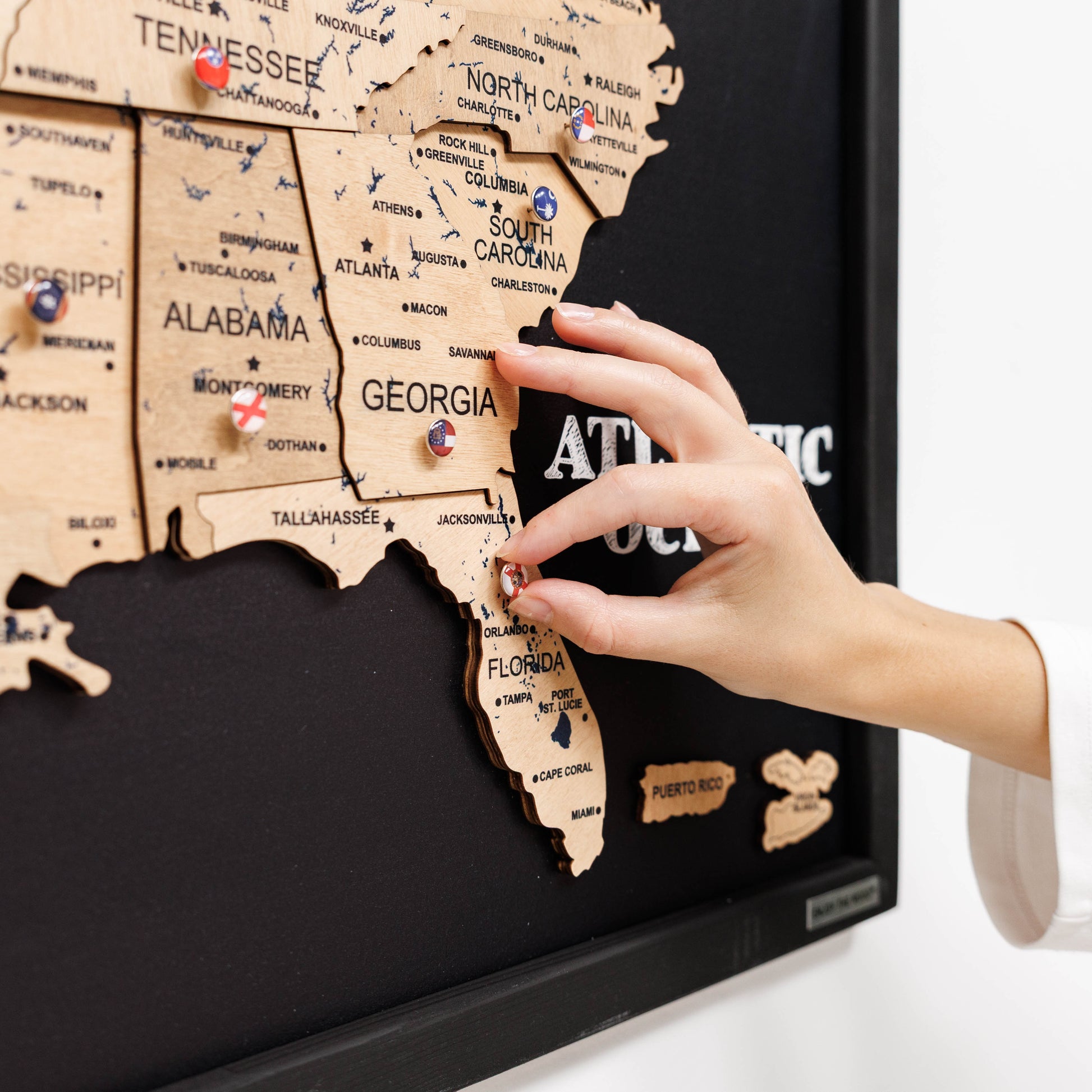 Hand placing a pin on a wooden map of the United States with a black background