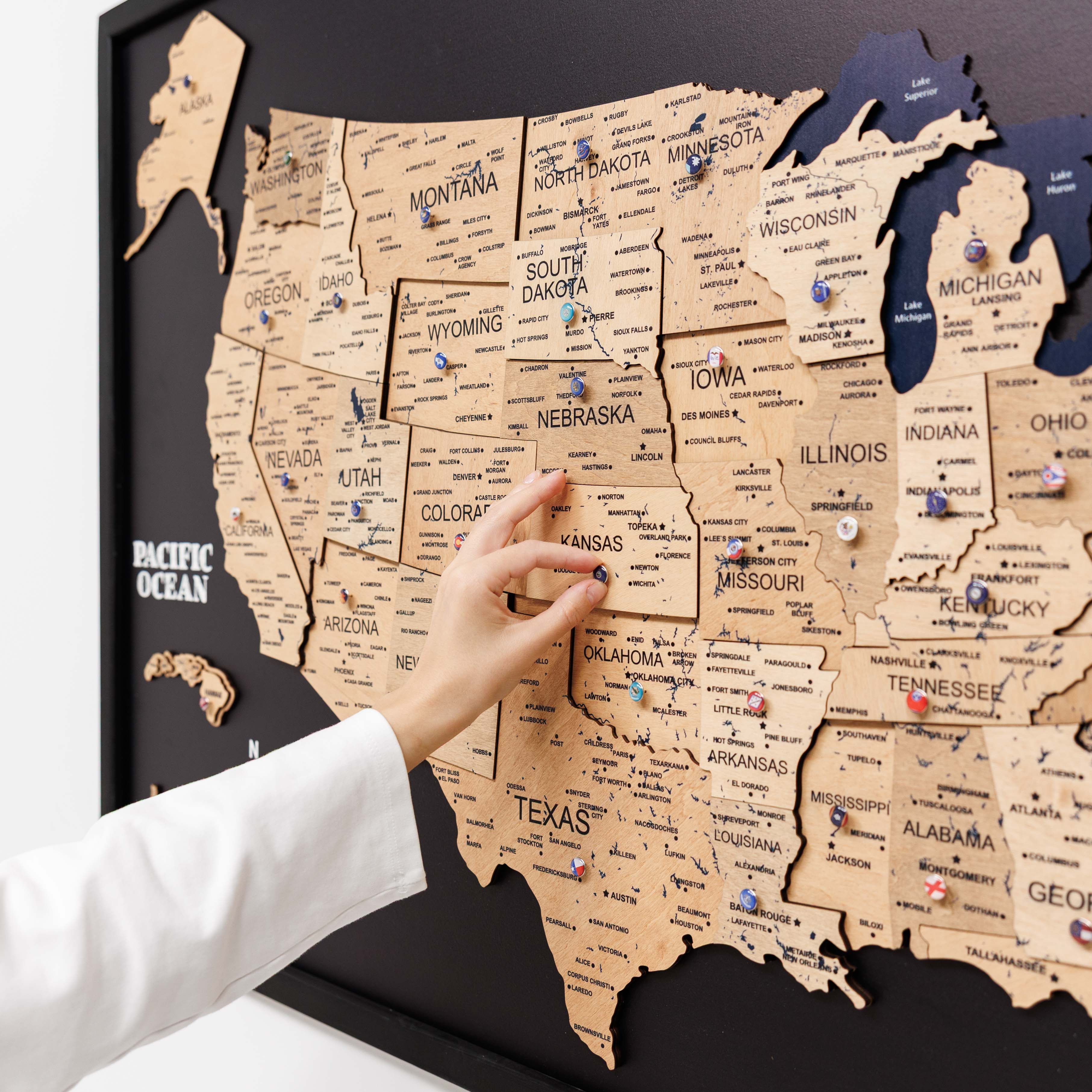 Map of the United States with pins marking locations, held by a person.