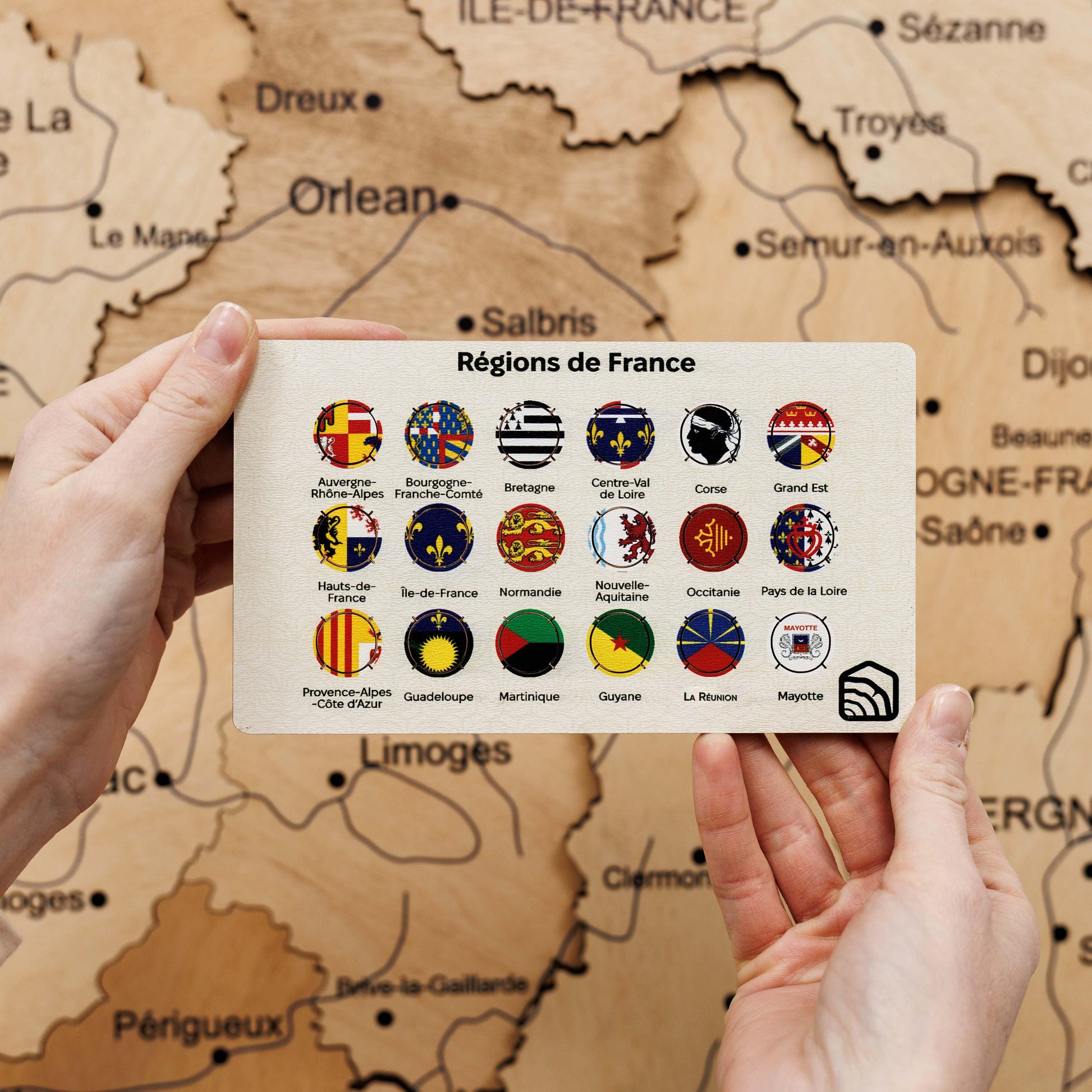 Map of France with regions displayed on a card held by hands against a map background.