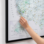 Person pinning a location on a map of the United States with pins already attached.