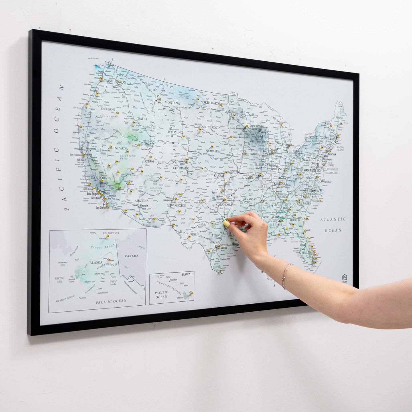 Person pointing at a map of the United States on a wall with a black frame.