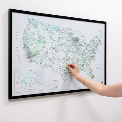 Person pointing at a map of the United States on a wall with a black frame.