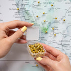 Hand holding a small container of gold beads with a map of the United States in the background.