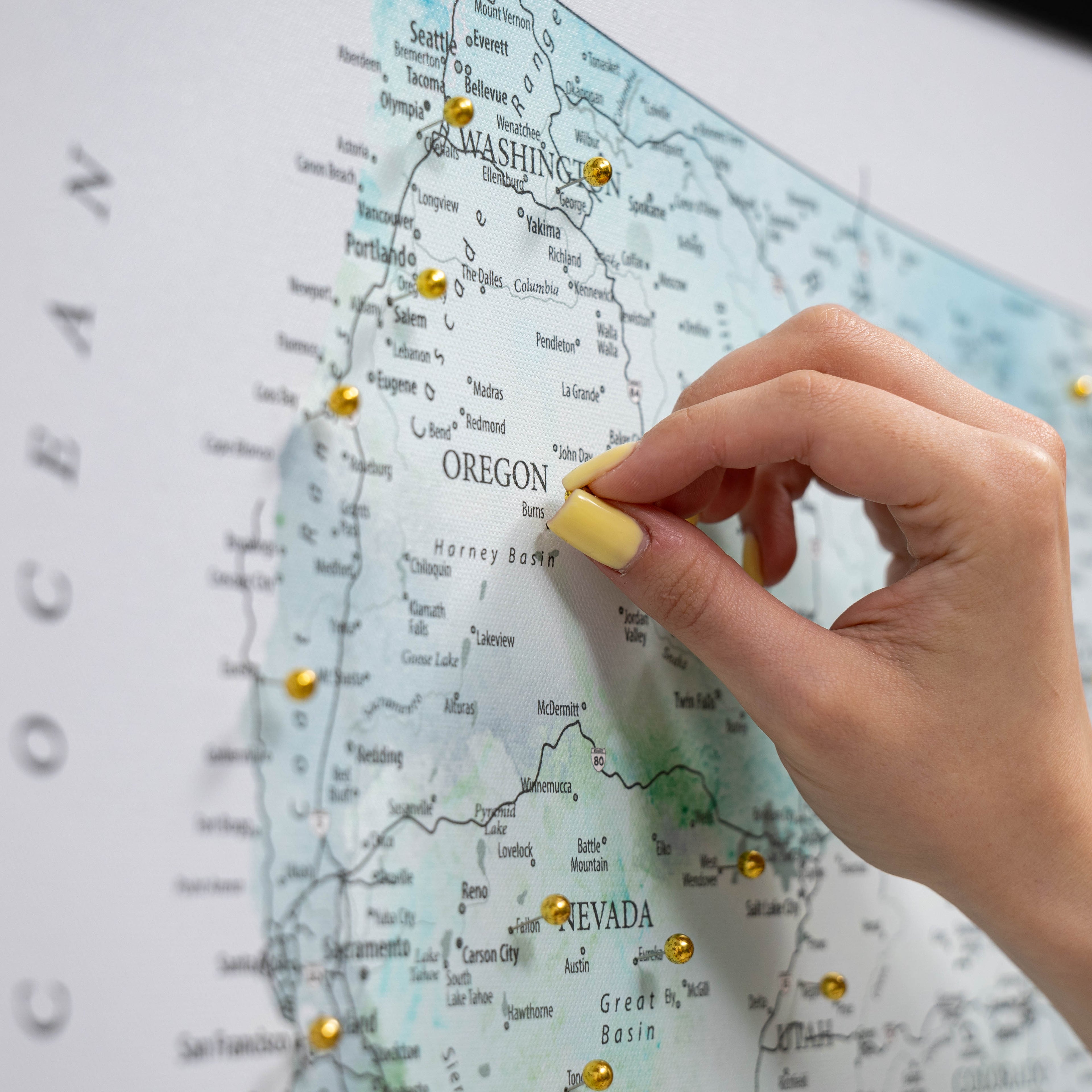 Hand placing a yellow pin on a map of the United States, focusing on Oregon.