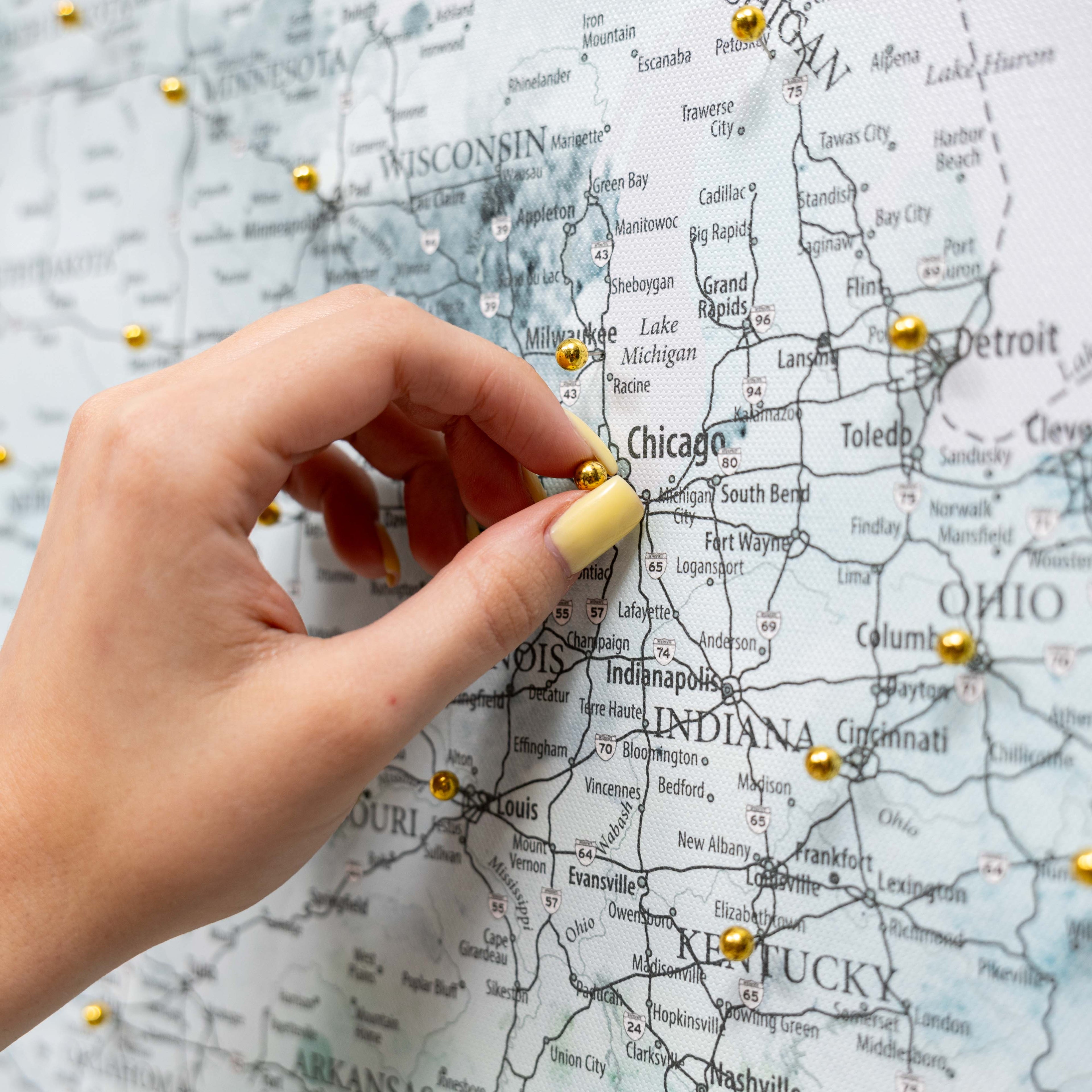 Hand placing a gold pushpin on a map of the United States, focusing on Indiana.