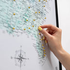Hand with yellow nail polish pinning a gold pushpin on a map