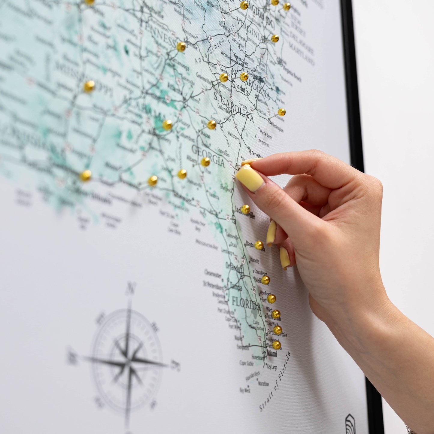 Hand with yellow nail polish pinning a gold pushpin on a map