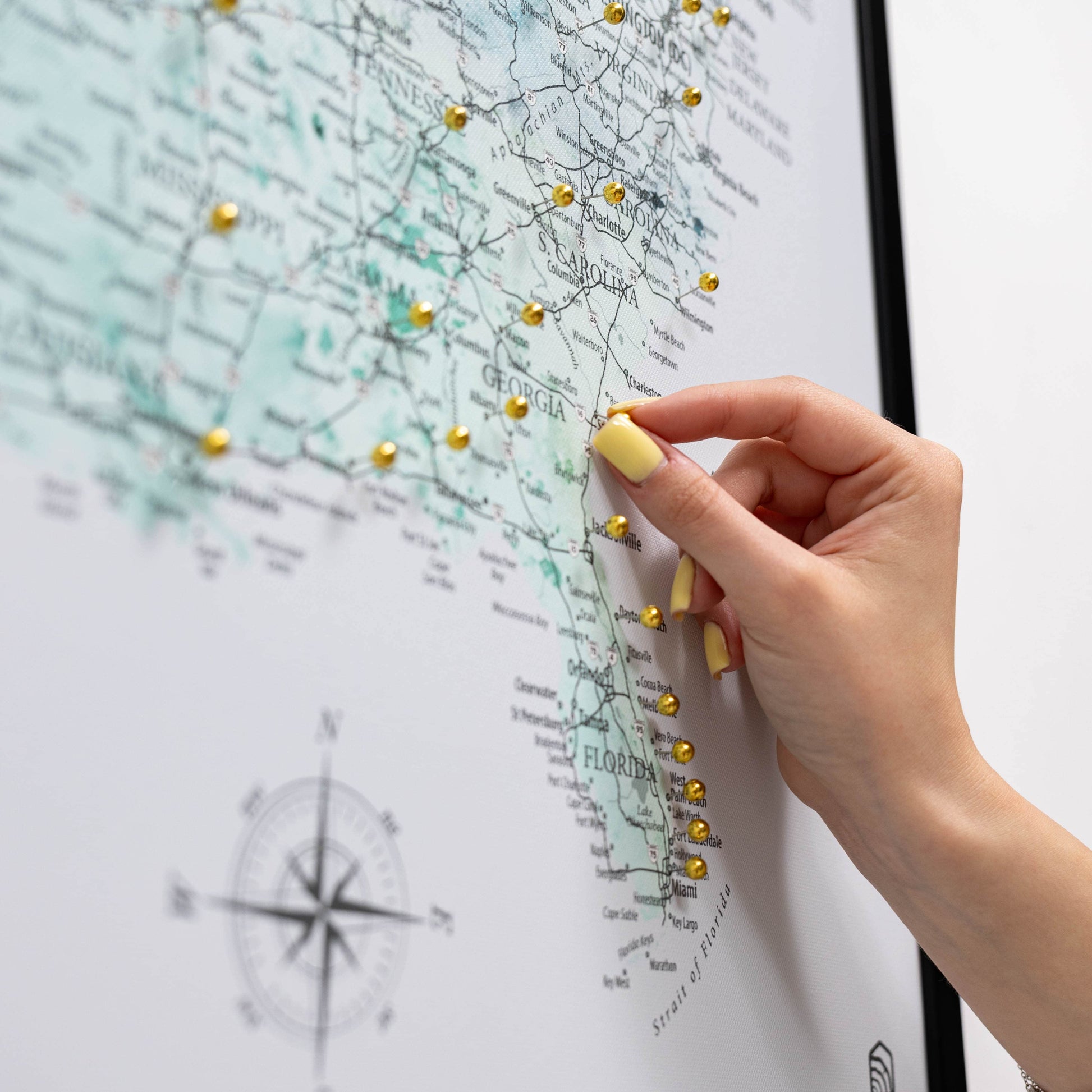 Hand with yellow nail polish pinning a gold pushpin on a map