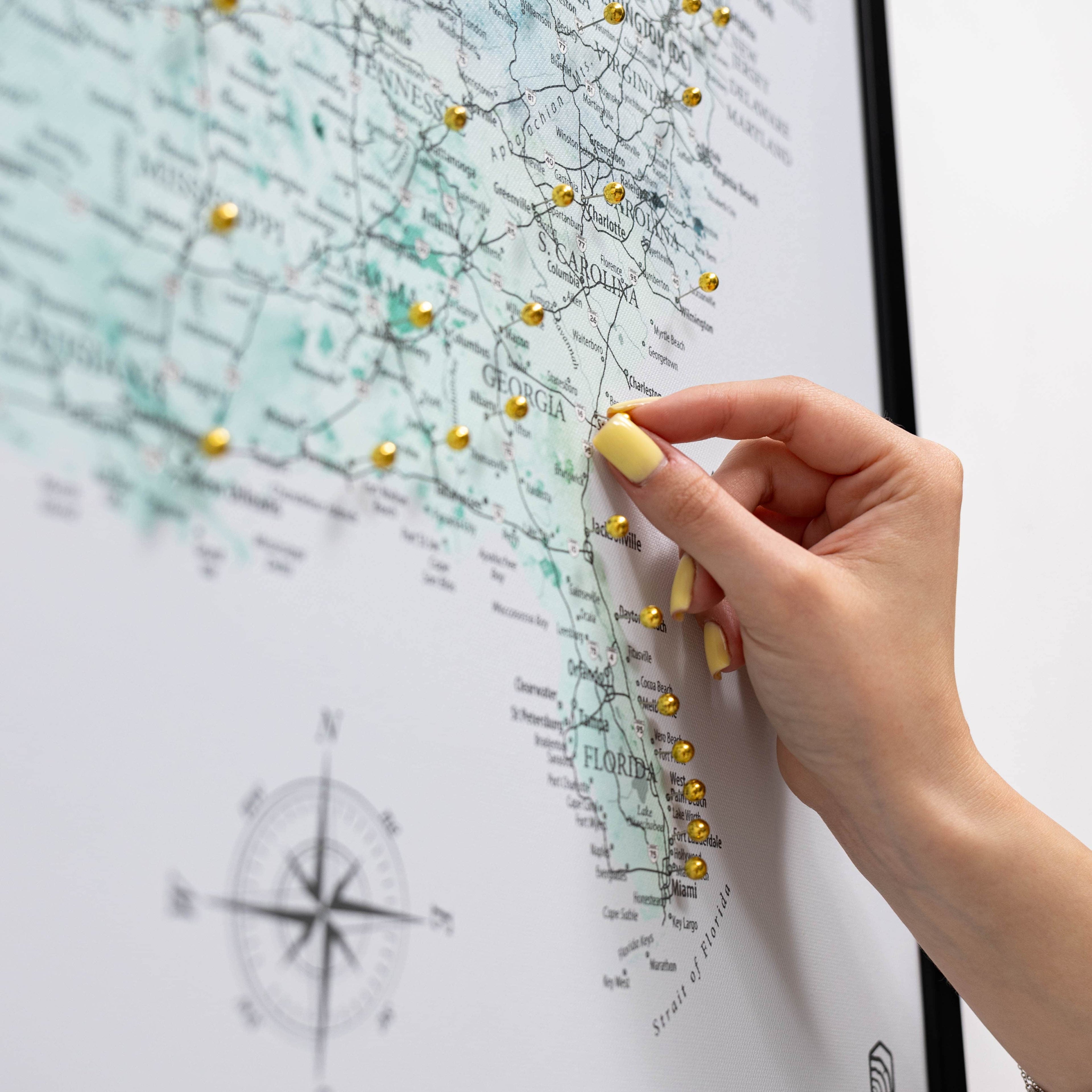 Hand with yellow nail polish pinning a gold pushpin on a map