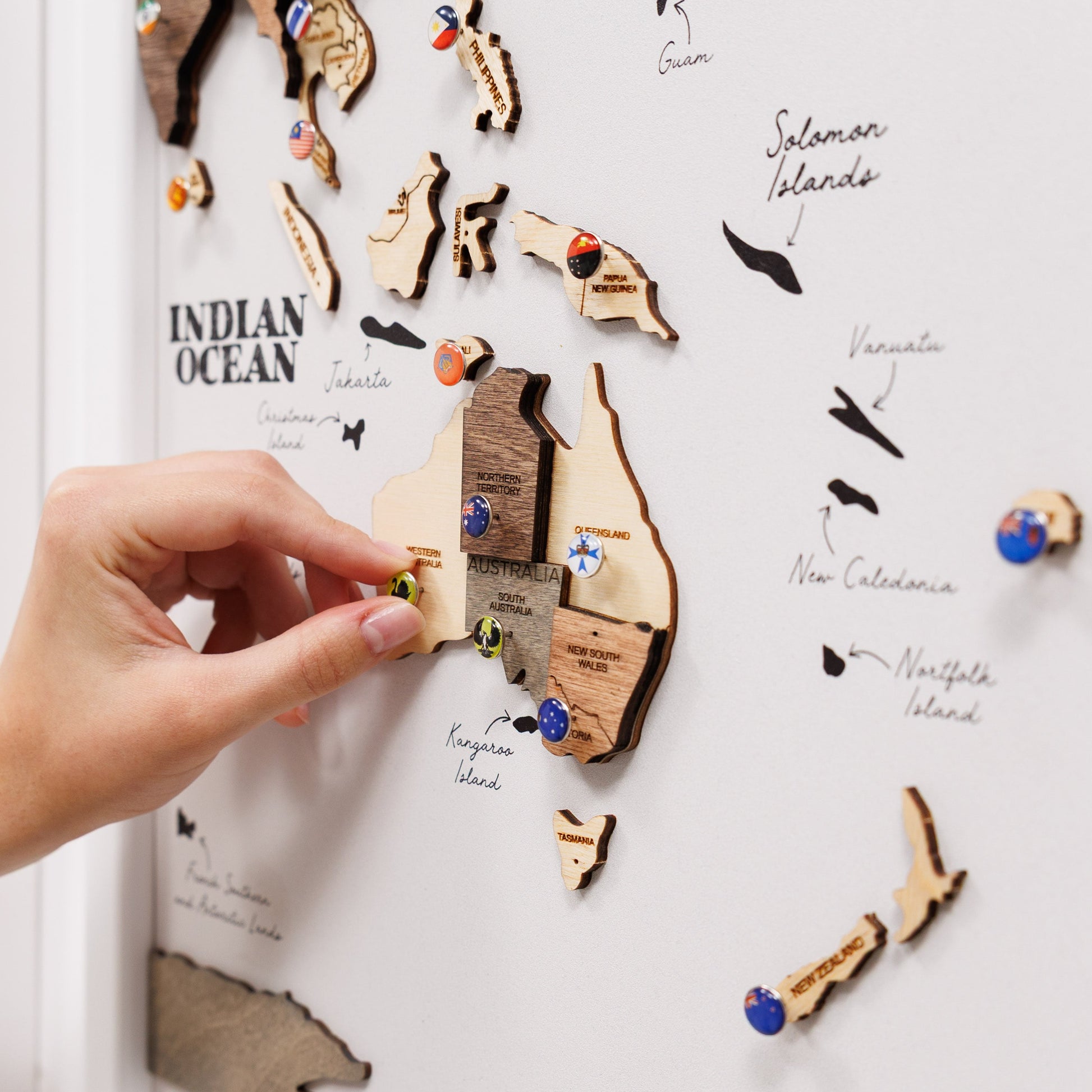 Wooden map magnets on a white board with a hand placing one of them.