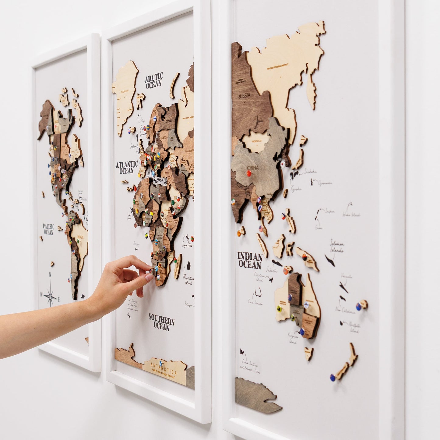 Wooden world map puzzle with a hand placing a piece on a white wall.