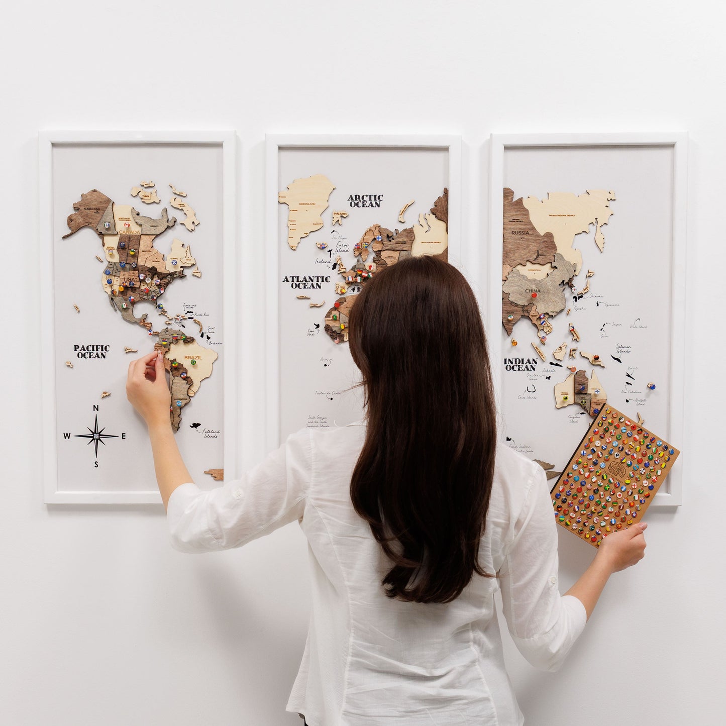 Woman assembling a wooden world map puzzle on a white wall.