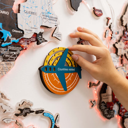Child's hand placing a 'Countries visited' travel tracker on a map of Canada.