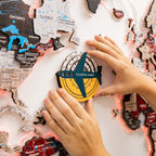 Person holding a 'Countries visited' badge over a world map puzzle