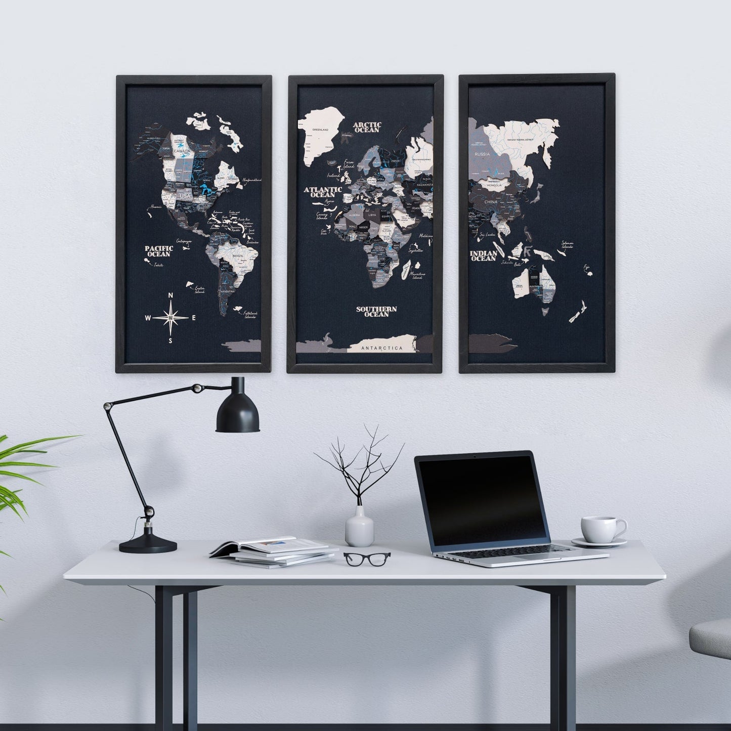 World map posters on a wall above a desk with a laptop and lamp.