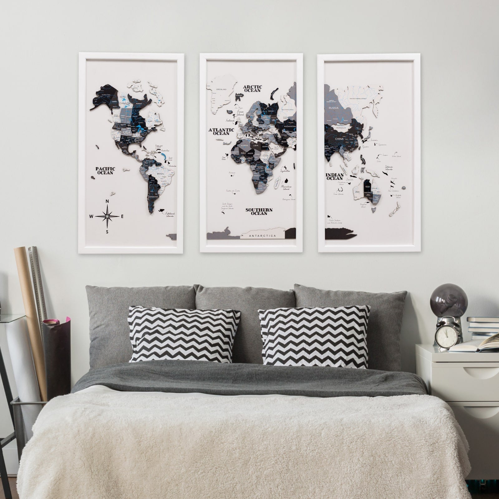 World map posters on a wall above a bed with gray bedding and black and white pillows.