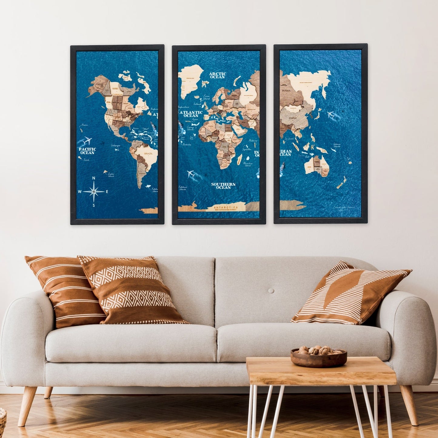 Three framed world maps on a wall above a sofa with decorative pillows.