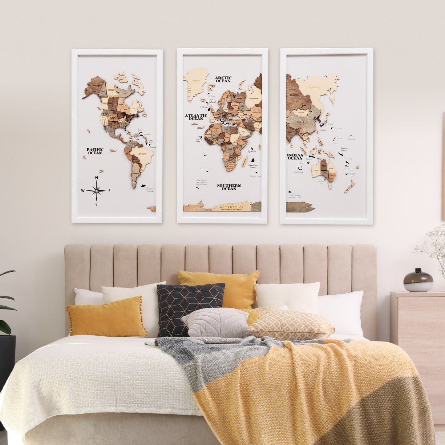 Three framed world maps on a wall above a bed with decorative pillows and a blanket.