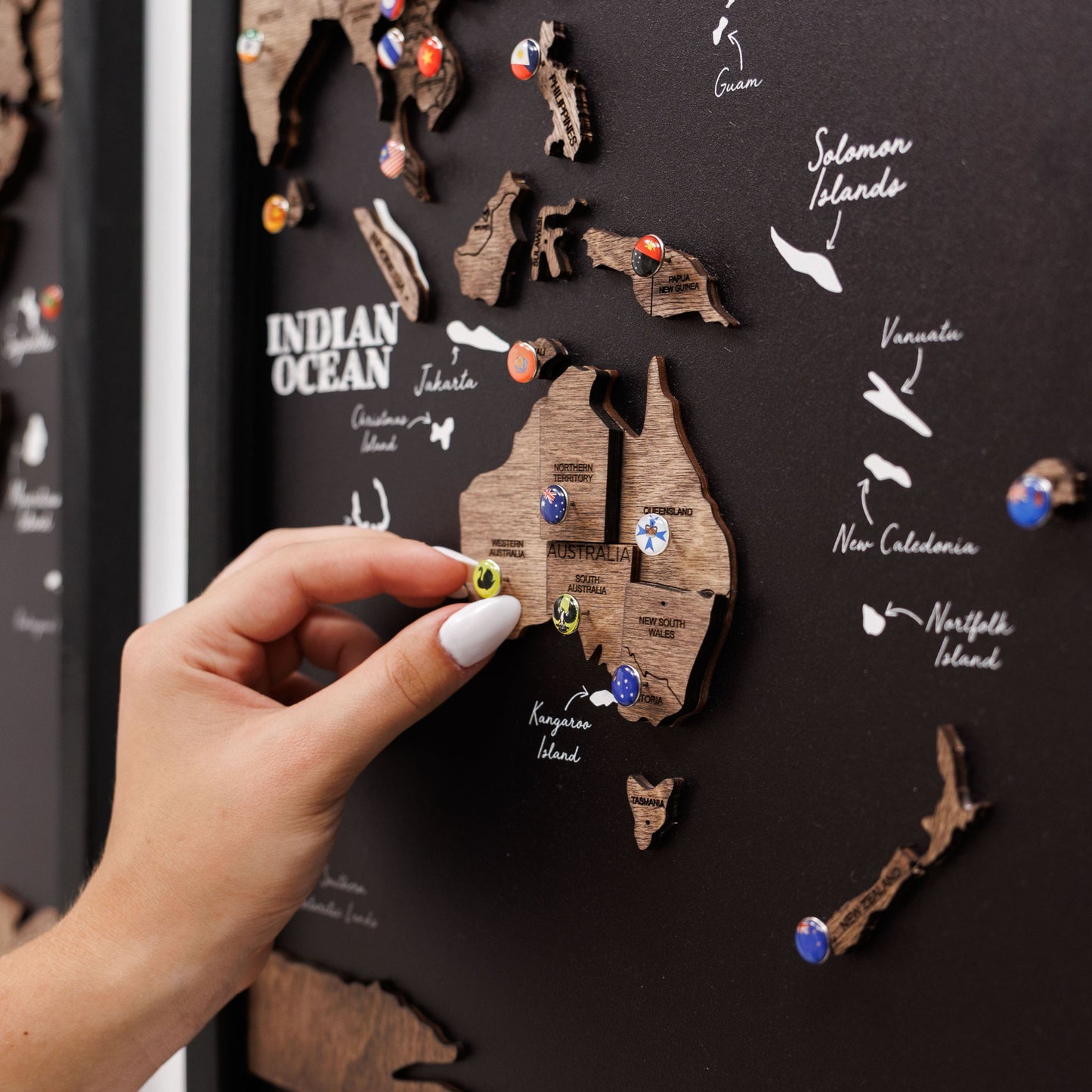 Hand placing a wooden Australia map on a black board with pinned locations.