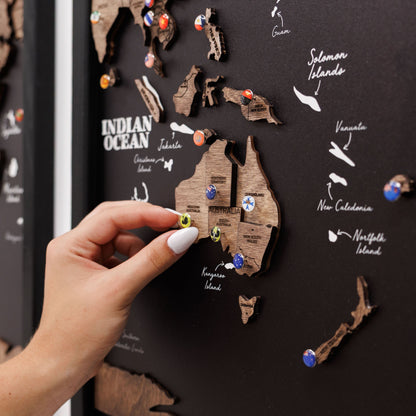 Hand placing a wooden Australia map on a black board with pinned locations.