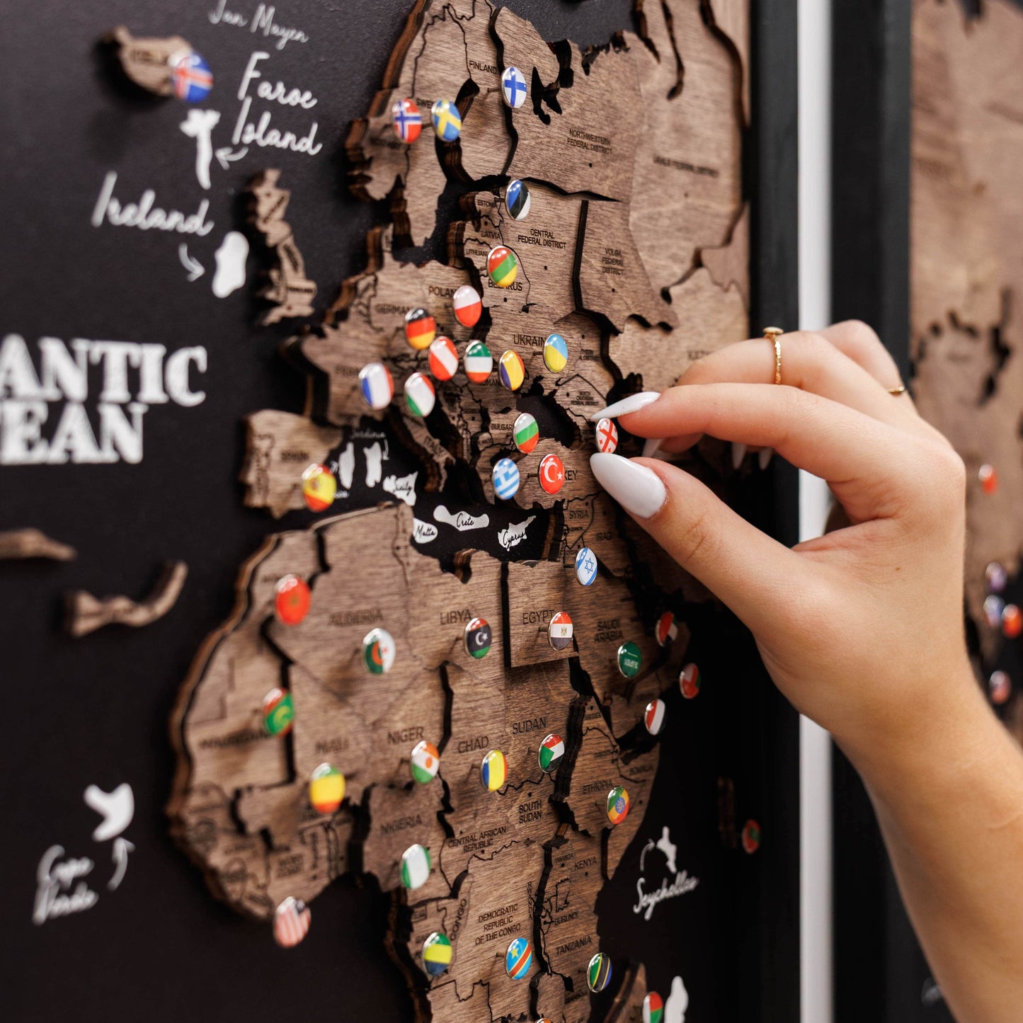 Hand placing a flag pin on a wooden map of Europe with pins representing various countries.
