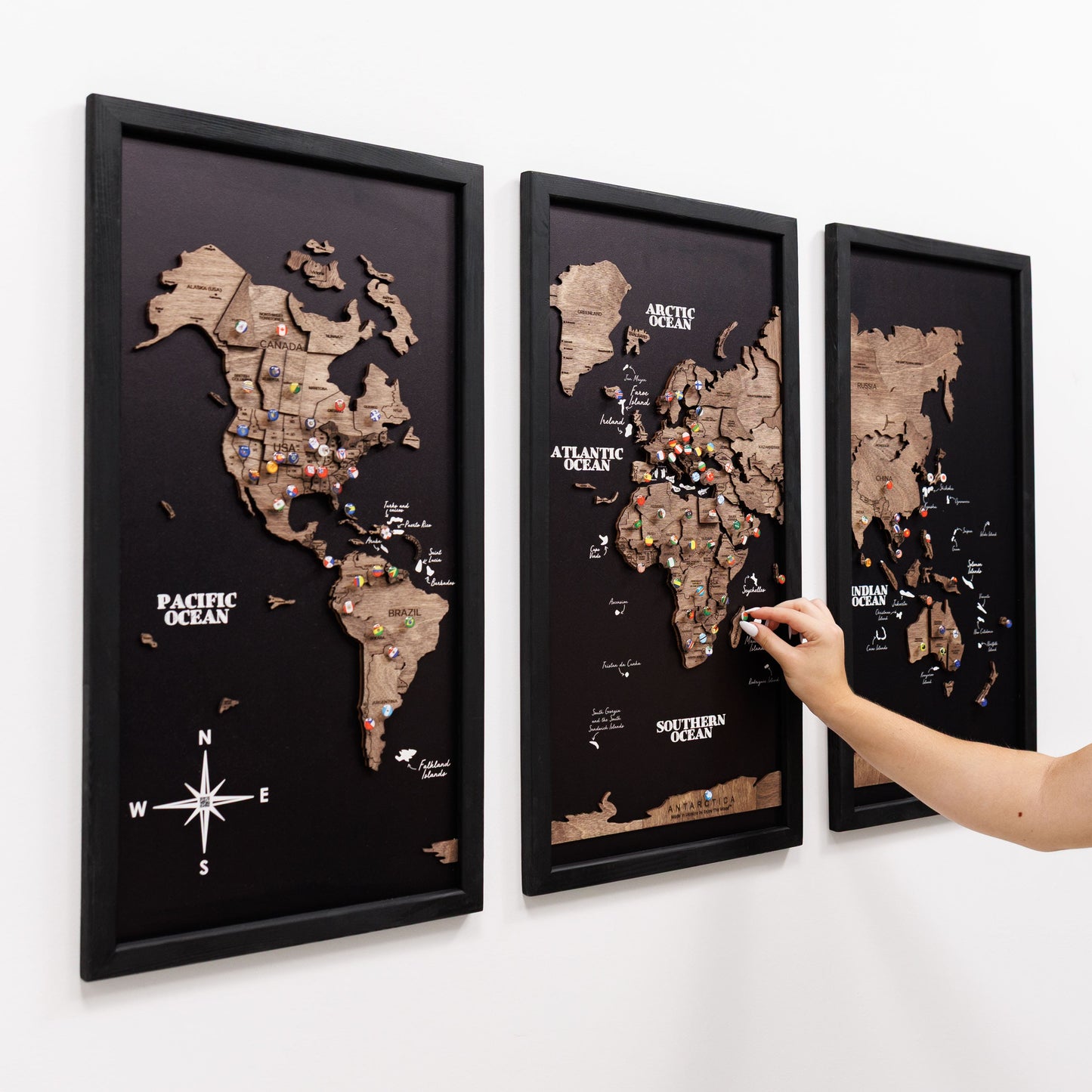 Three framed world maps on a wall with a hand pointing to one of them.