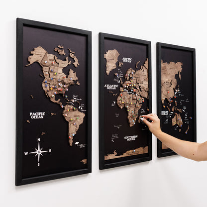Three framed world maps on a wall with a hand pointing to one of them.
