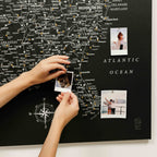 Map of the United States with pins and a person holding photos on a black background