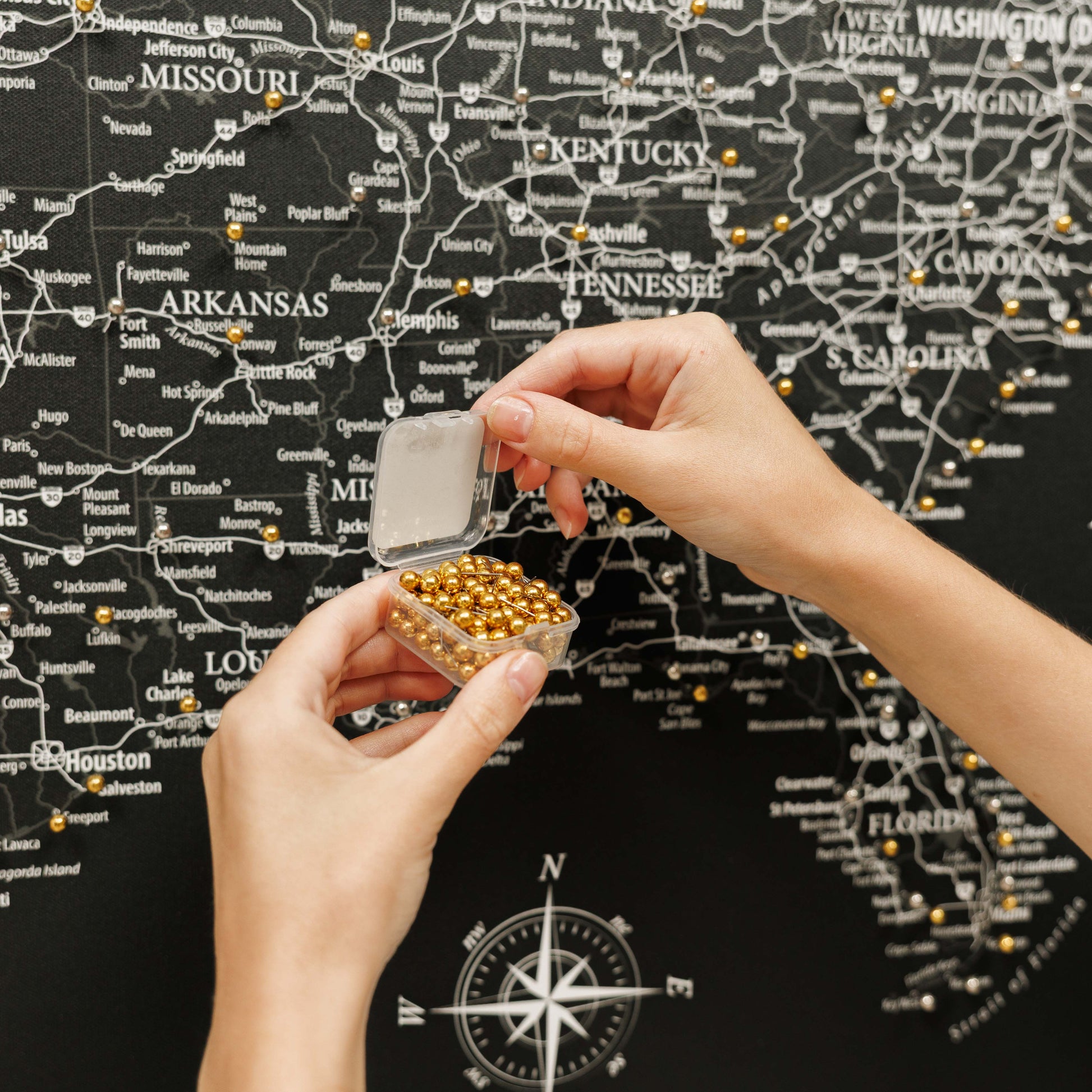 Person holding a small container of gold beads in front of a map