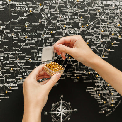 Person holding a small container of gold beads in front of a map